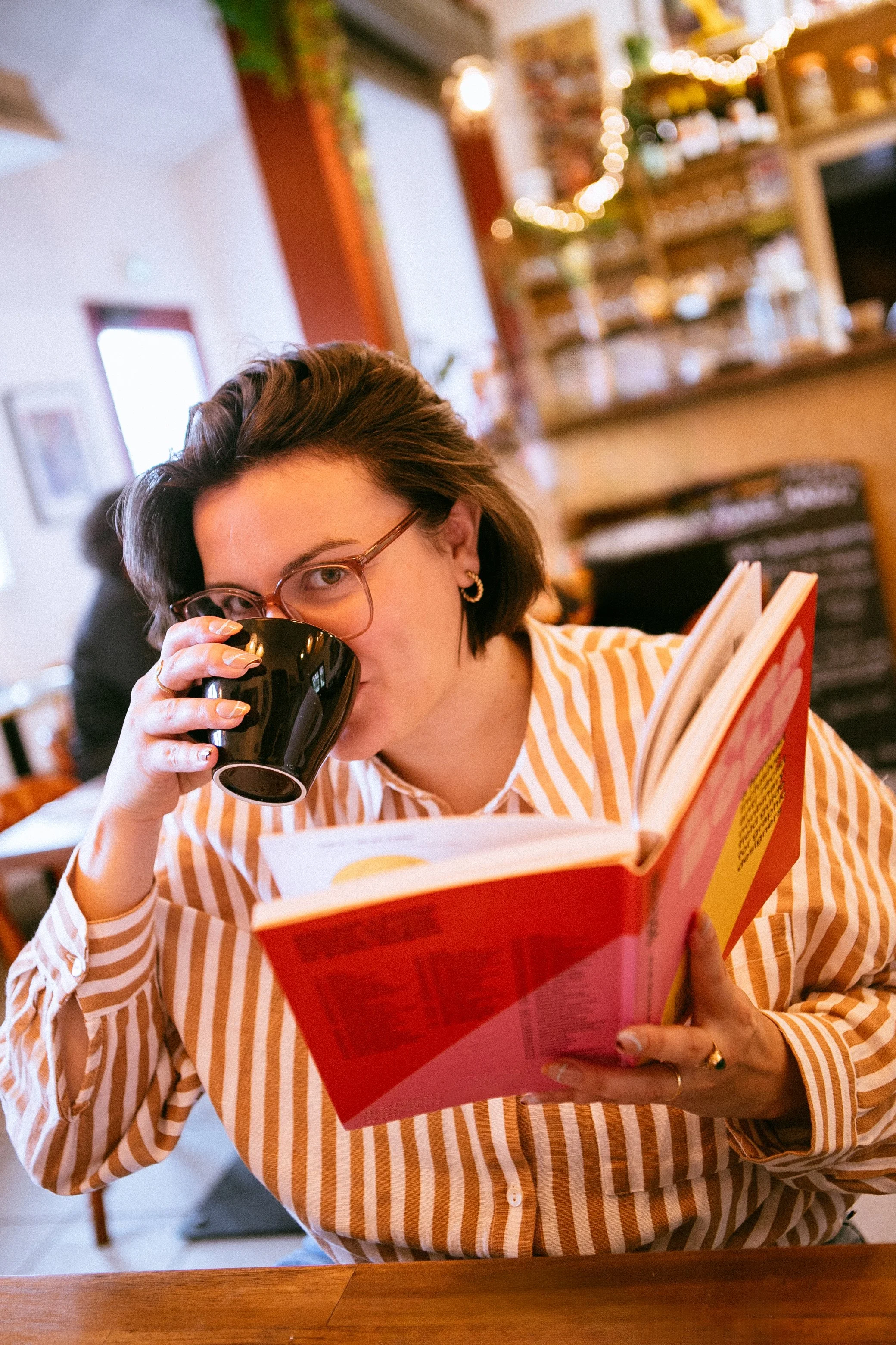 Hello Loup boit une tasse de café avec une main, un livre sur le design dans l'autre main