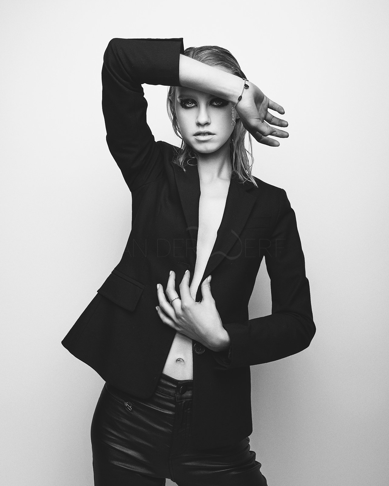 Schwarz-Weiß-Foto einer jungen Frau mit kurzen Haaren, die eine schwarze Jacke trägt, und eine Hand liegt an ihrer Taille, die andere Hand ist über ihr Gesicht gehoben.