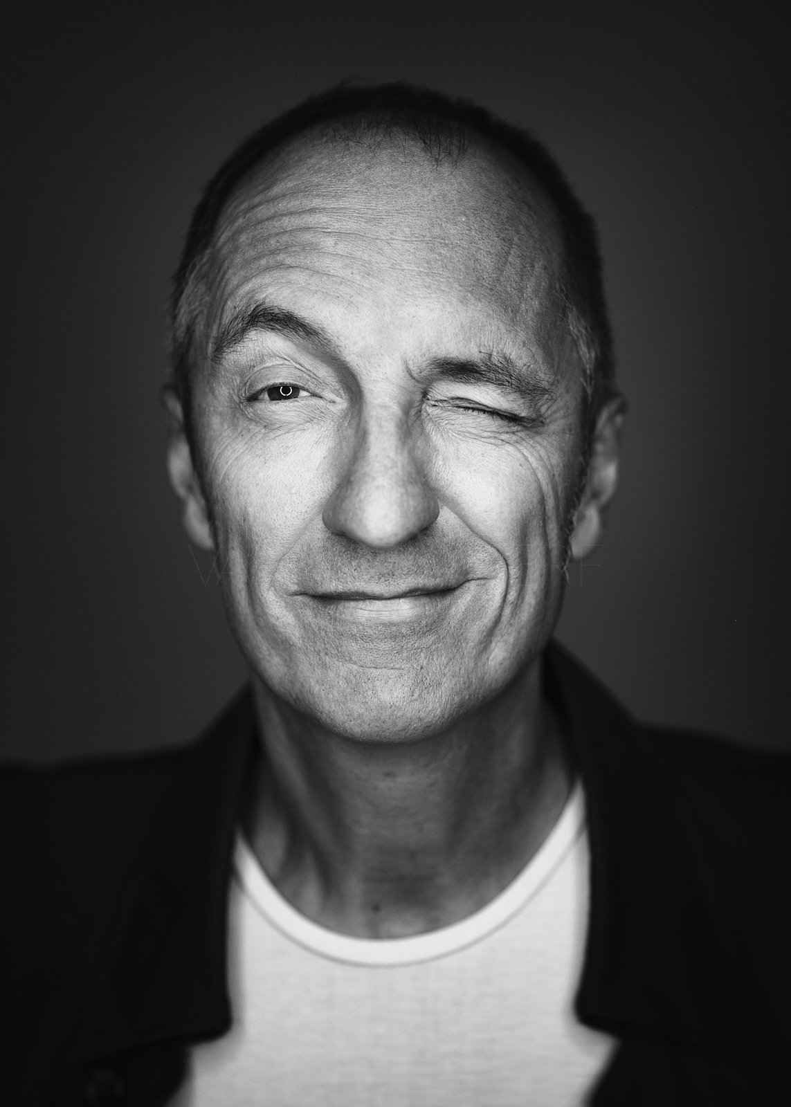 Schwarz-weiß Porträt eines Mannes, der lachend mit einem Augenzwinkern in die Kamera schaut.