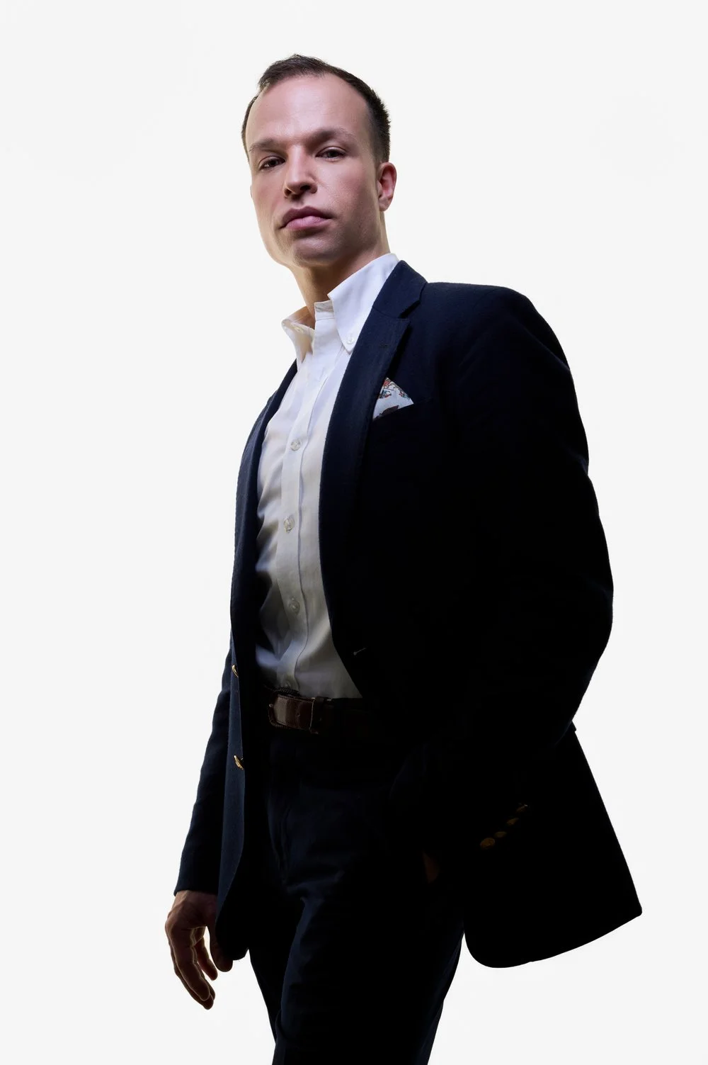 Junge Mann in dunklem Anzug mit weißen Hemd, stehend vor hellem Hintergrund.