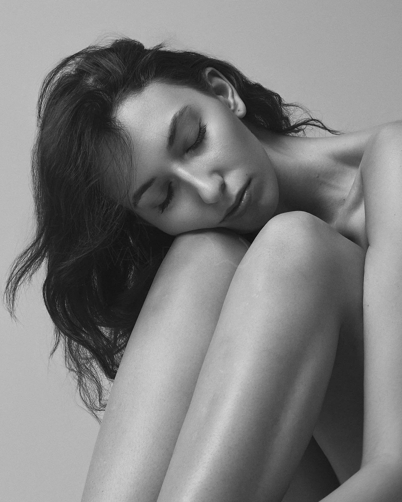 Schwarz-weiß-Fotografie einer jungen Frau mit geschlossenen Augen, die ihren Kopf auf ihr Knie legt.