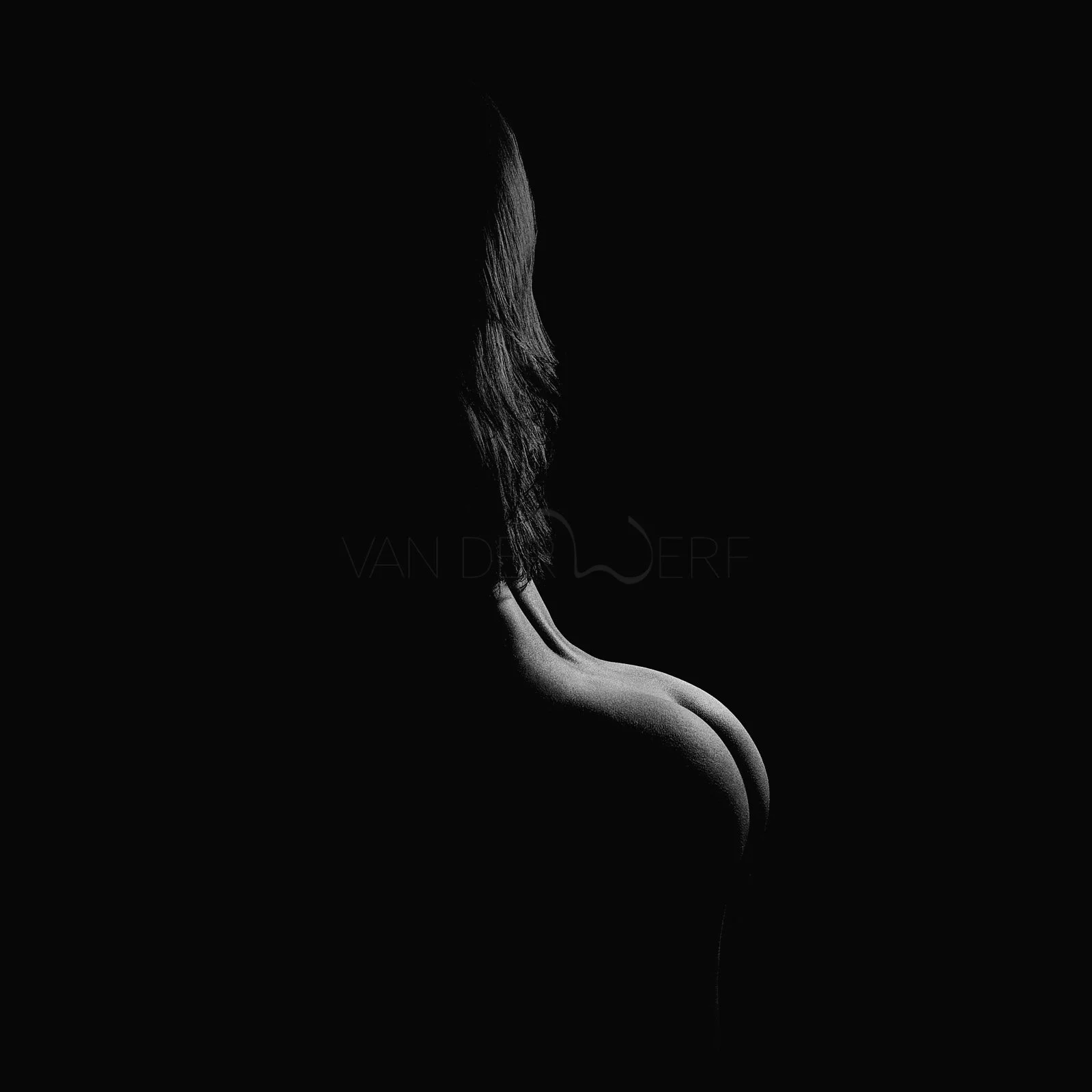 Schwarzes und weißes Bild einer Frau, die von hinten mit nur einem Teil ihres Gesichts und ihrer Schulter sichtbar ist. Der Hintergrund ist schwarz, und das Licht hebt die Konturen ihrer Schulter und ihrer Haare hervor.