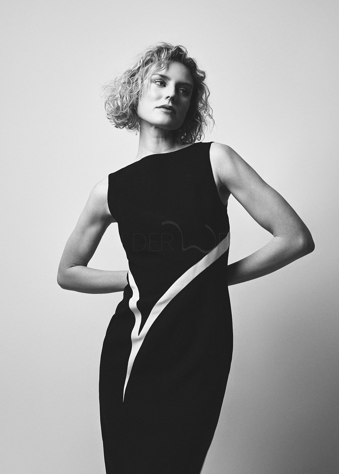 Schwarz-weiß-Fotografie einer Frau mit kurzen, lockigen Haaren, die eine elegante, ärmellose schwarze Kleider trägt und nach links blickt