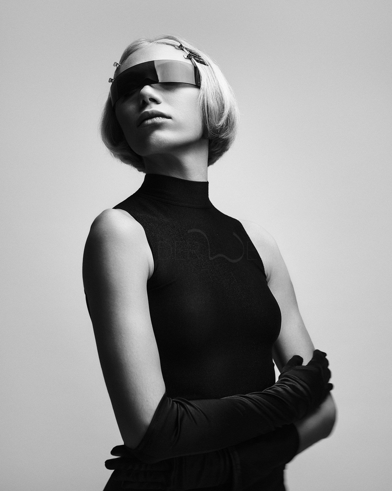 Schwarz-Weiß-Foto einer stilvollen Frau mit Kurzhaarfrisur, die eine futuristische Augenmaske trägt und einen schwarzen Ärmelrock trägt.