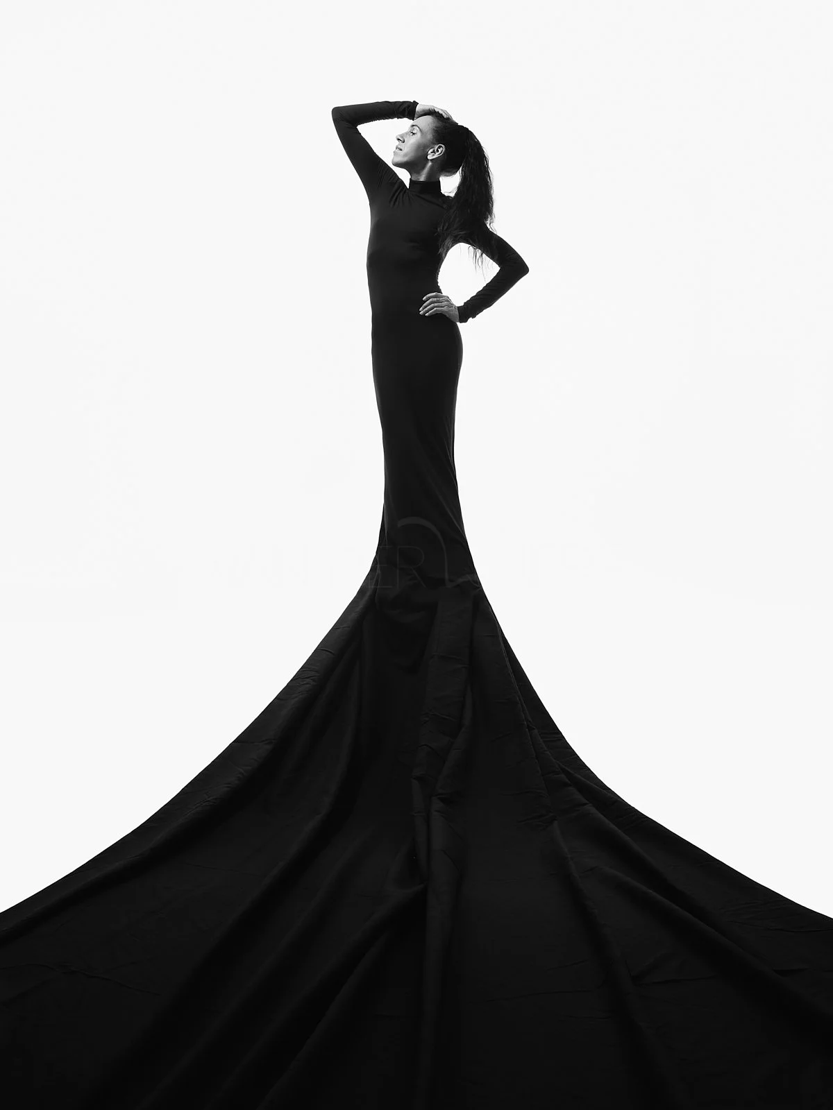 Schwarzes Kleid an einer Frau, die auf einem weißen Hintergrund steht, während sie nach oben schaut, mit ihrer Hand auf der Stirn, in monochromatischer Aufnahme.