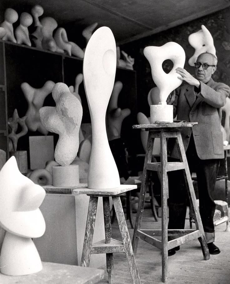 Artist crafting abstract sculptures in studio, surrounded by various organic shapes on stands and shelves.
