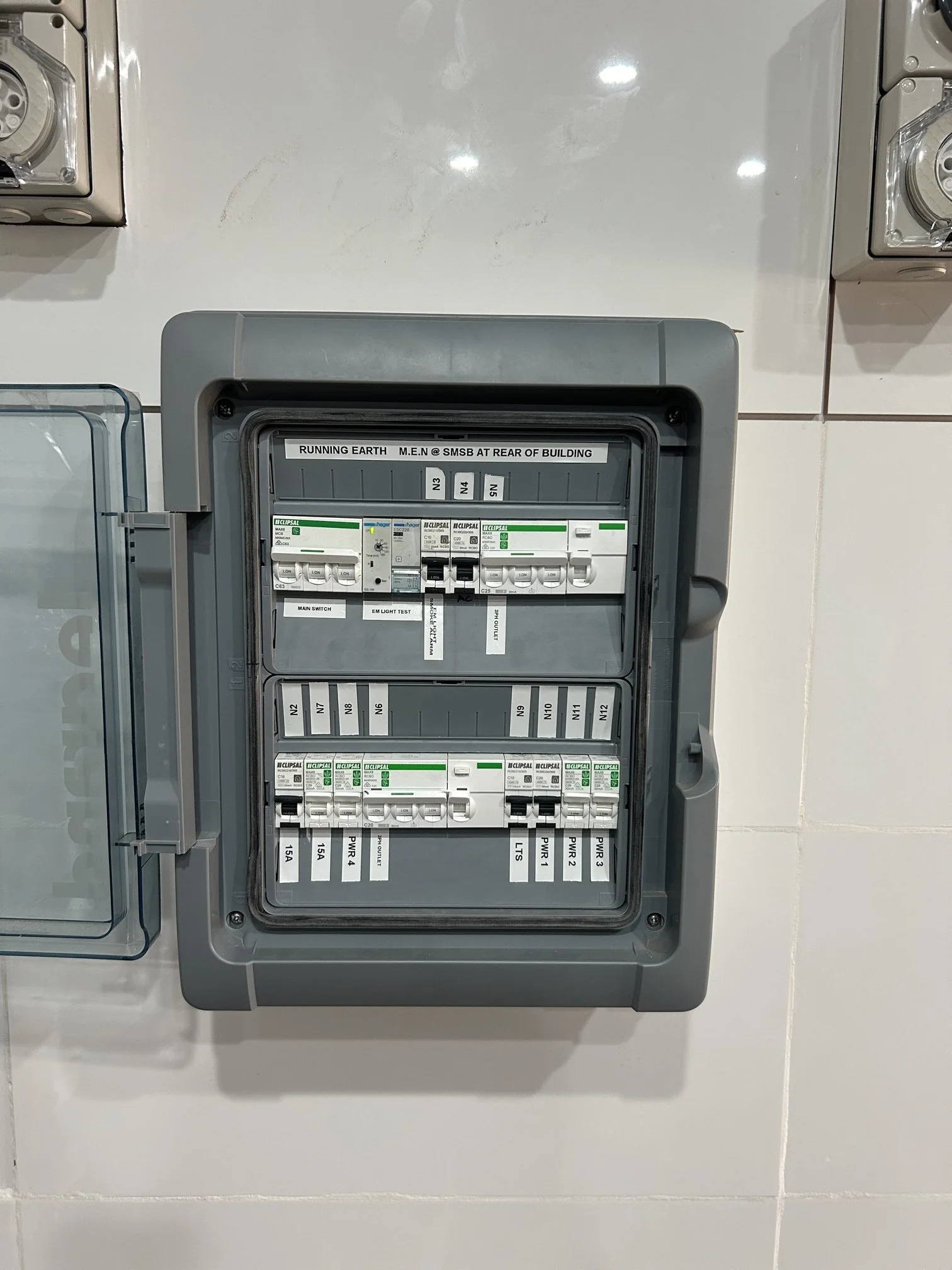 Electrical breaker panel with multiple switches and labels on a white tiled wall.