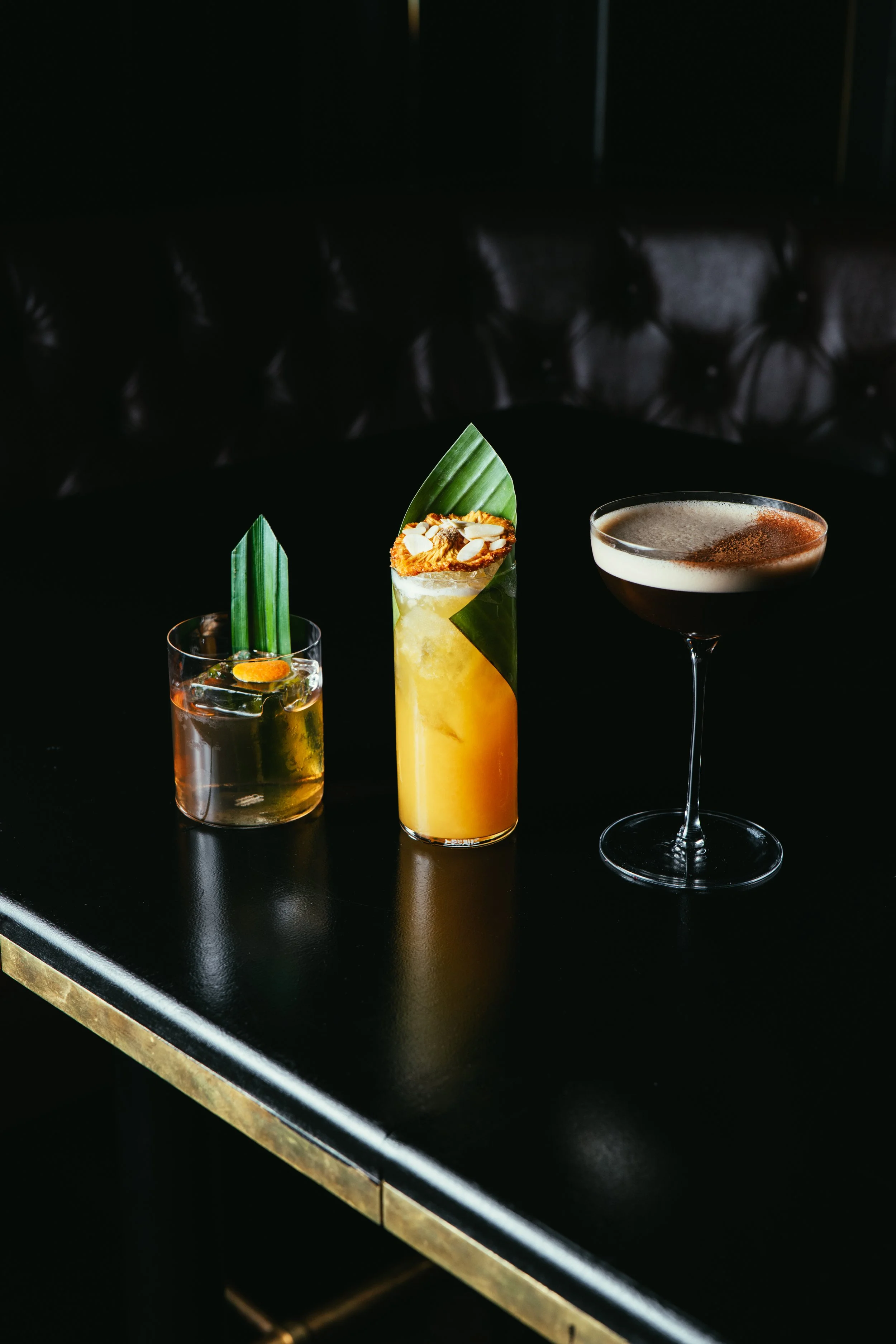 Three styled cocktails on a black table in a dark setting.