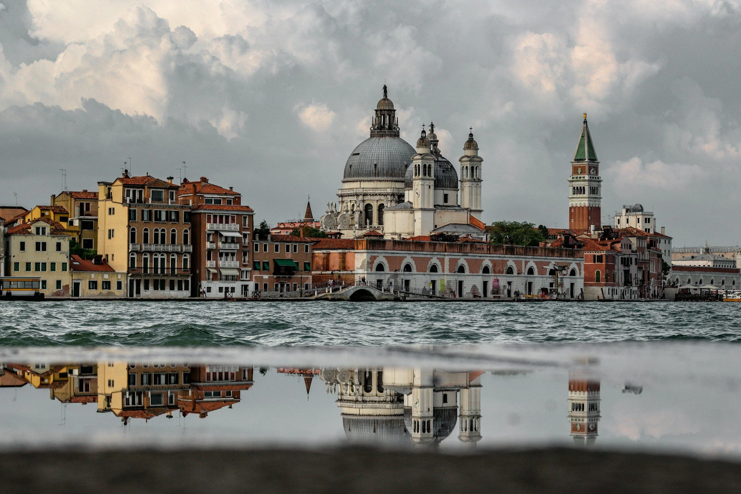 Stadtansicht von Venedig mit markanten Gebäuden und Wasser im Vordergrund, reflektiert im Wasser.