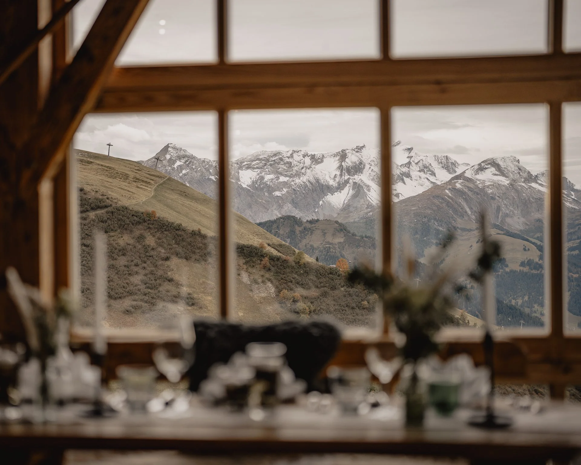Berglandschaft mit schneebedeckten Gipfeln, gesehen durch ein Fenster eines Gebäudes mit Holzrahmen.