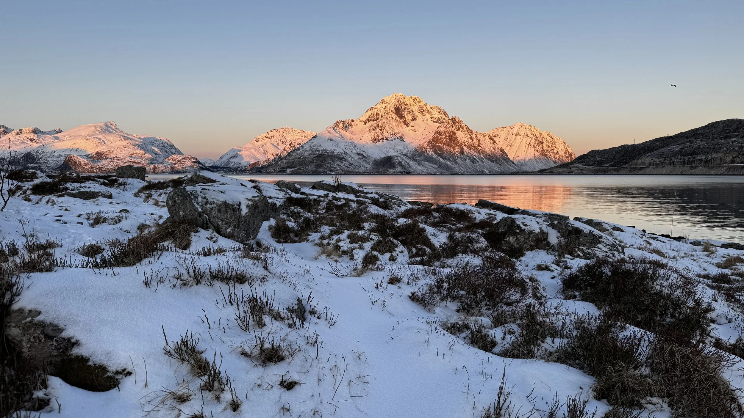 Schneebedecktes Ufer mit Bergen im Sonnenuntergang und ruhigem Wasser