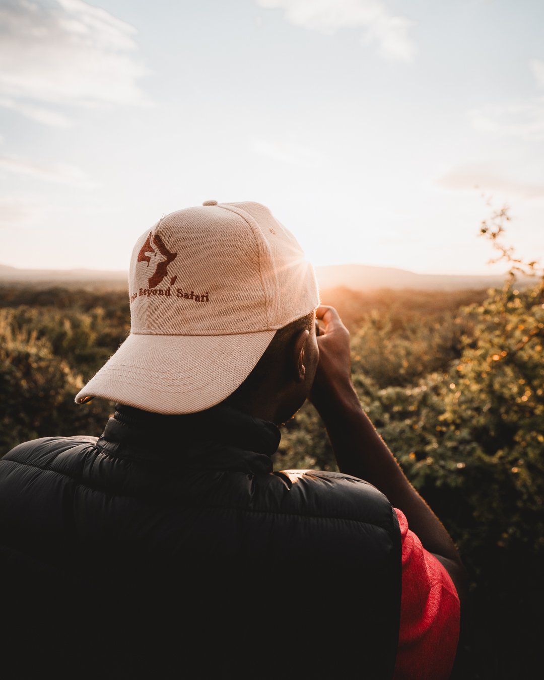 Person mit Baseballkappe und Kamera fotografiert Landschaft bei Sonnenuntergang.