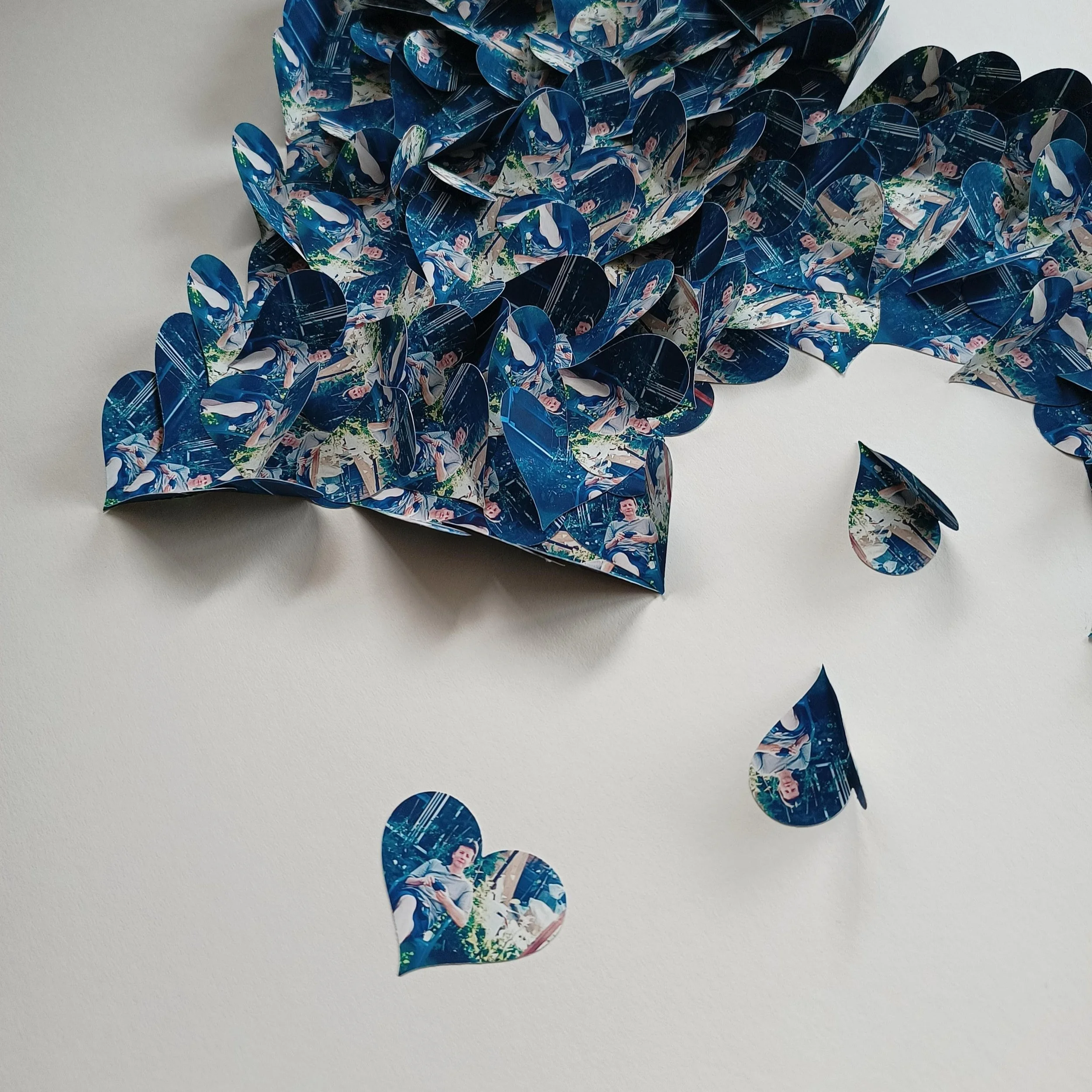 Decorative paper cutouts of hearts with printed images on a white background, arranged to resemble a broken heart.