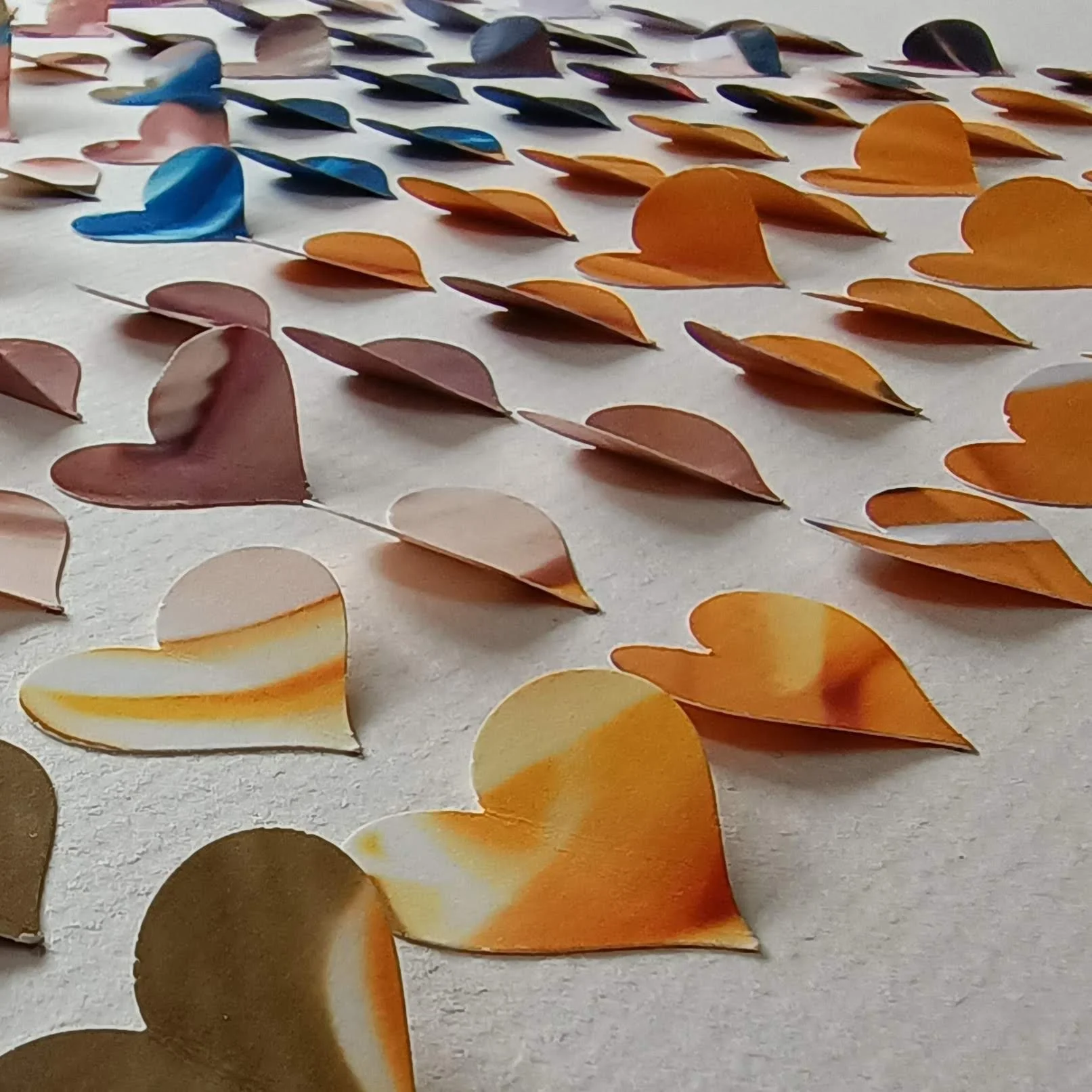 Colorful paper hearts arranged on a flat surface in rows, with colors including brown, orange, yellow, pink, and blue.