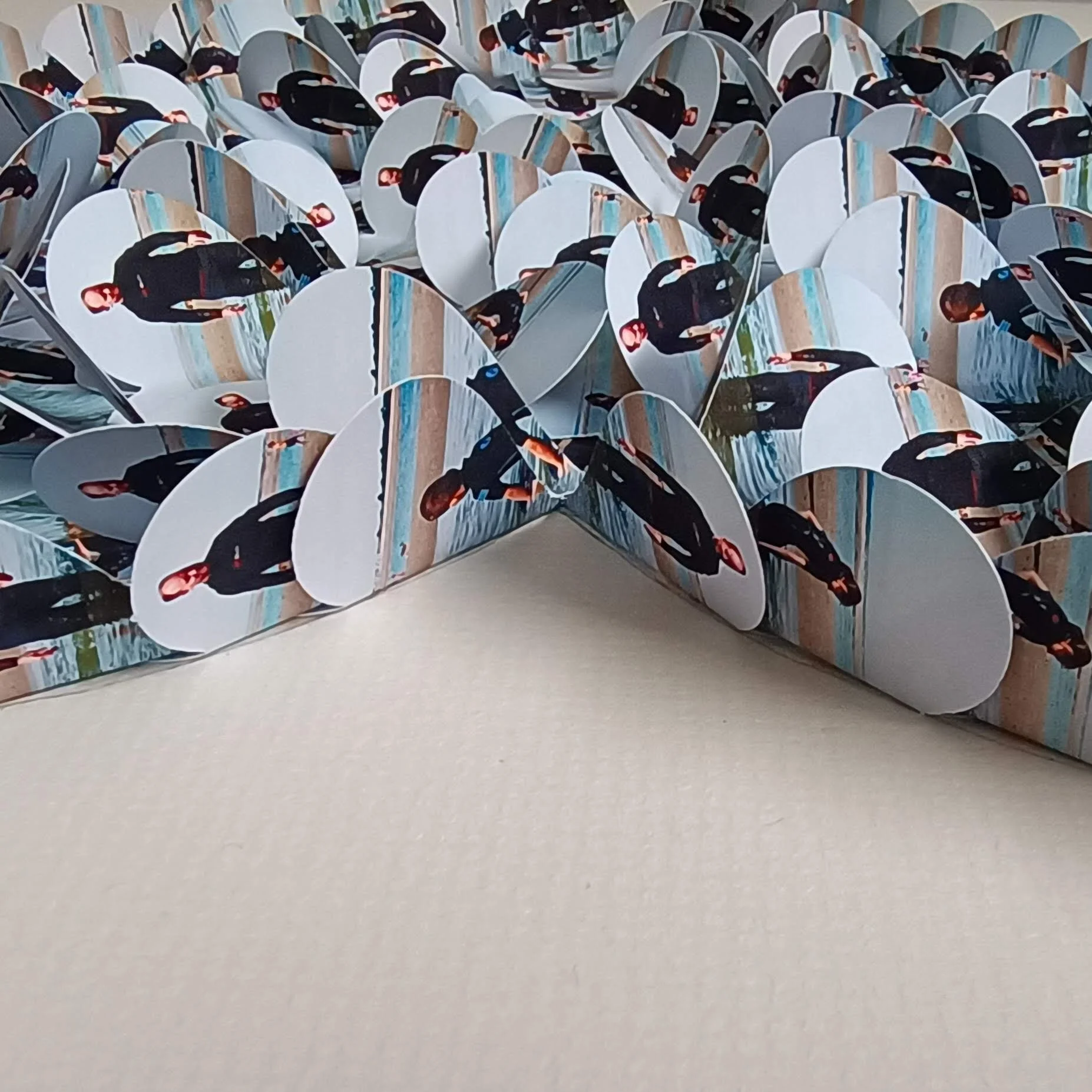 Paper hearts with printed images of a man wearing a black suit walking along a beach, arranged in a 3D layered pattern.