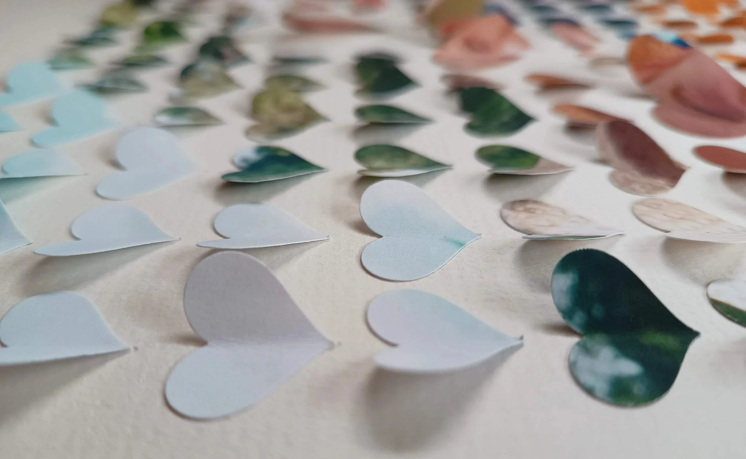 Assorted paper or hearts in pastel blue, white, pink, and green colors scattered on a light surface.