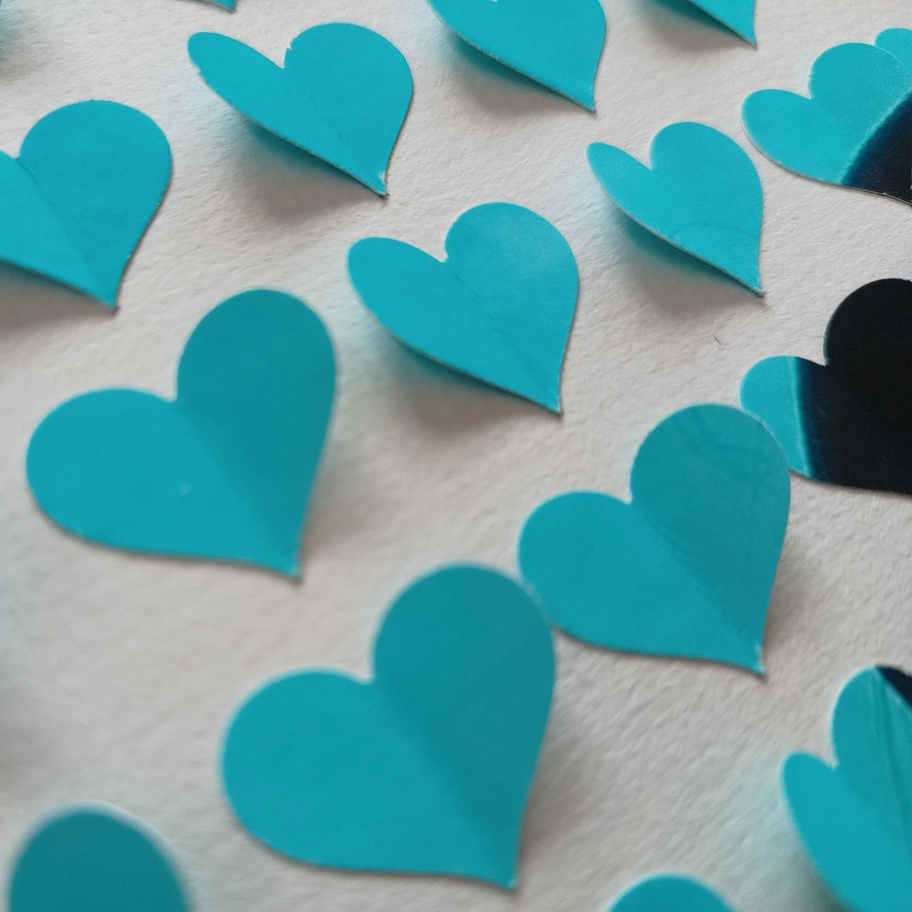 Multiple blue paper hearts scattered on a white surface.
