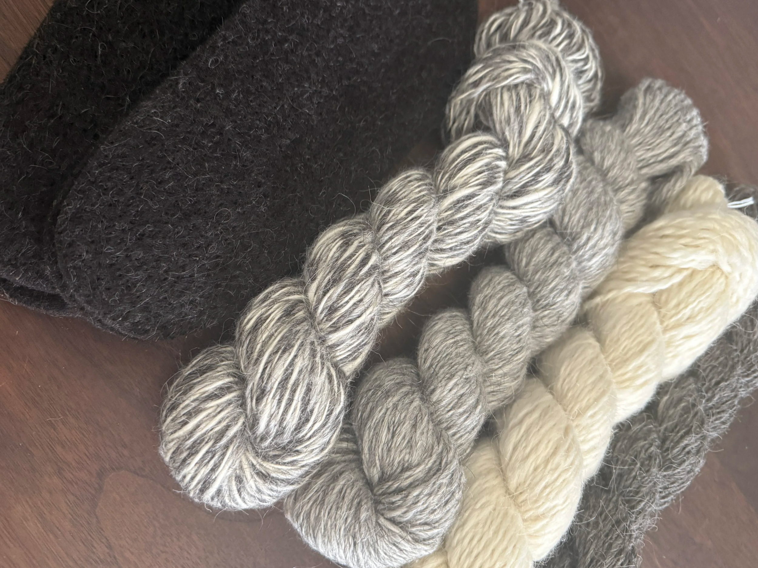 Close-up of three hanks of Icelandic wool yarn in silver, gray, and cream colors next to black Icelandic wool boot inserts.