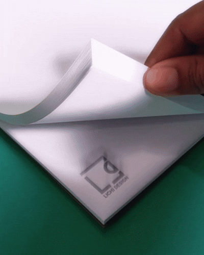 A hand peeling a sheet of white paper from a stack, revealing part of a printed logo underneath.