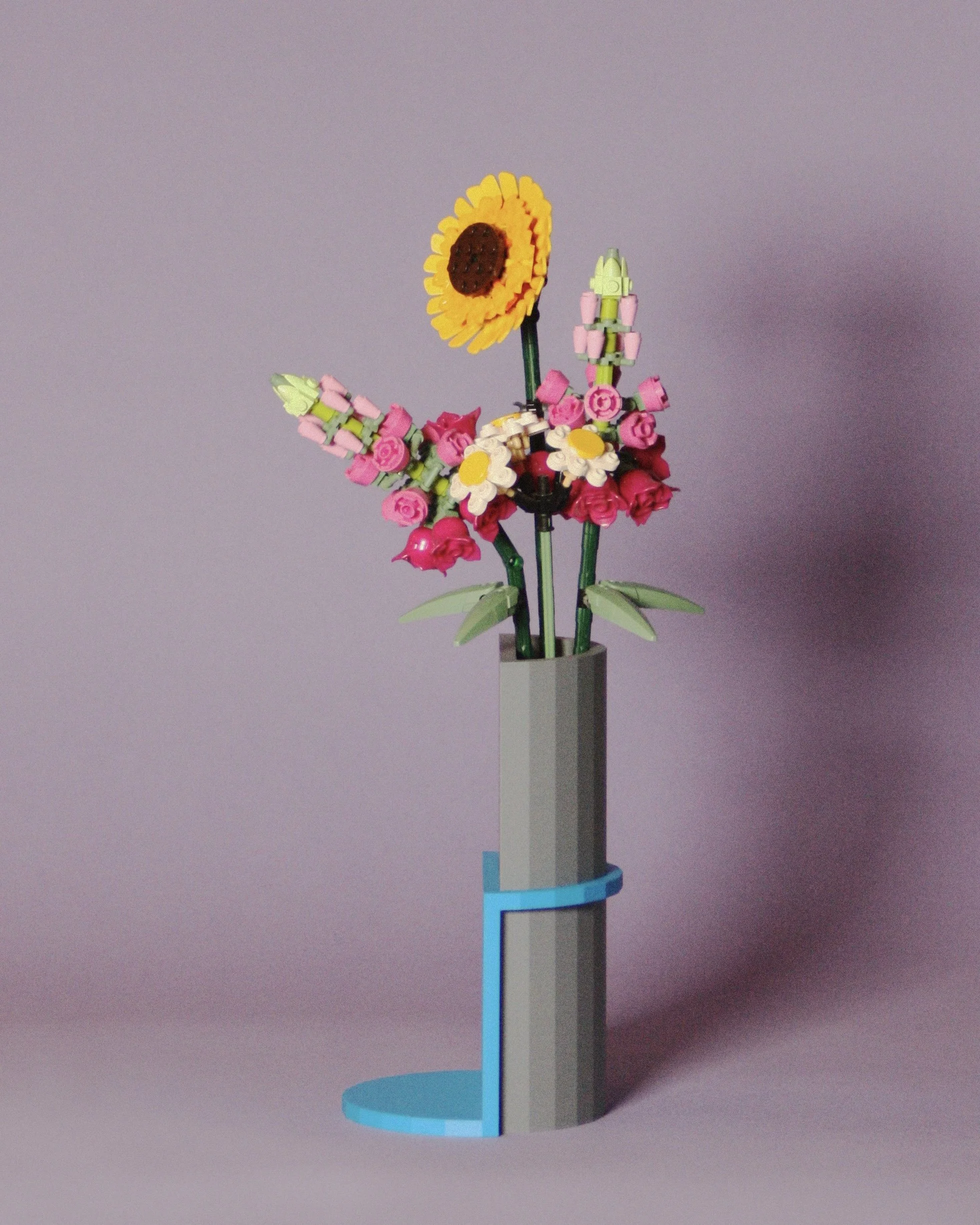 A LEGO flower bouquet with sunflowers, daisies, and pink flowers in a tall gray LEGO vase on a pink background.