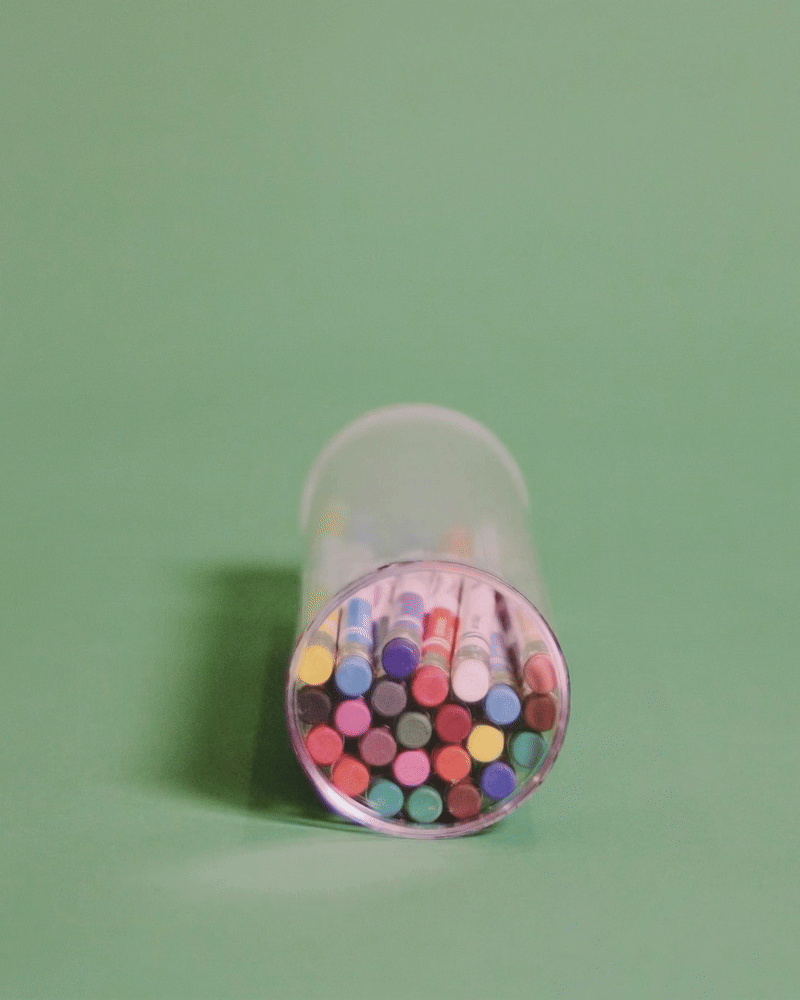 A transparent container filled with colorful markers on a green surface.