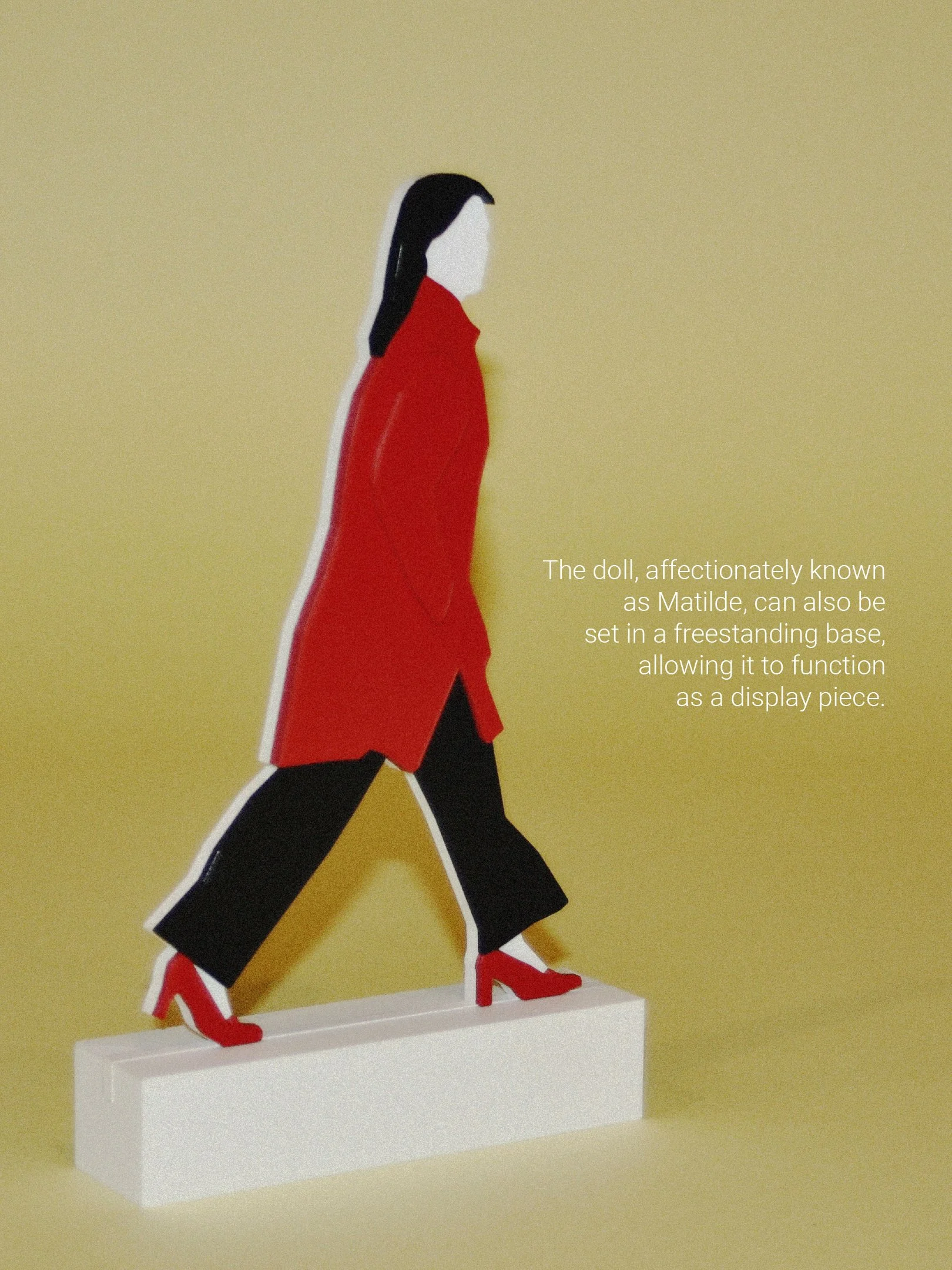 A stylized doll resembling Matilde, wearing a red coat, black pants, and red high heels, mounted on a white freestanding base against a light yellow background.