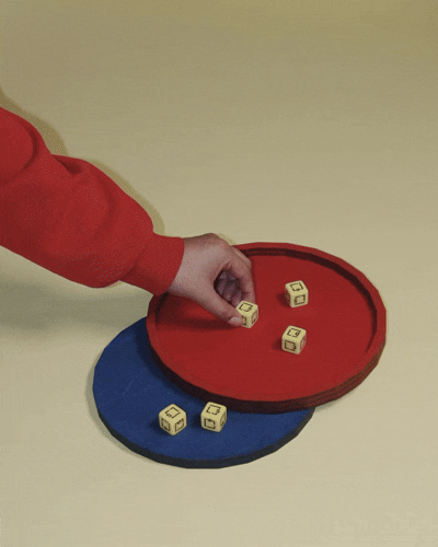 Child's hand reaching for lettered dice on red and blue circular trays.