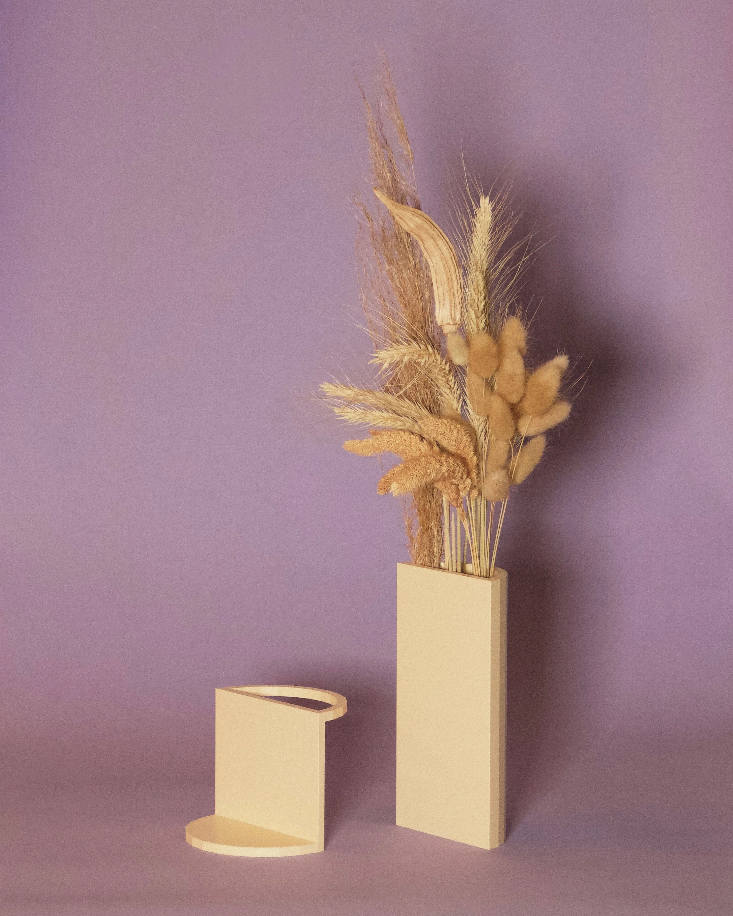 Arrangement of dried grasses and wheat in a beige vase against a purple background.