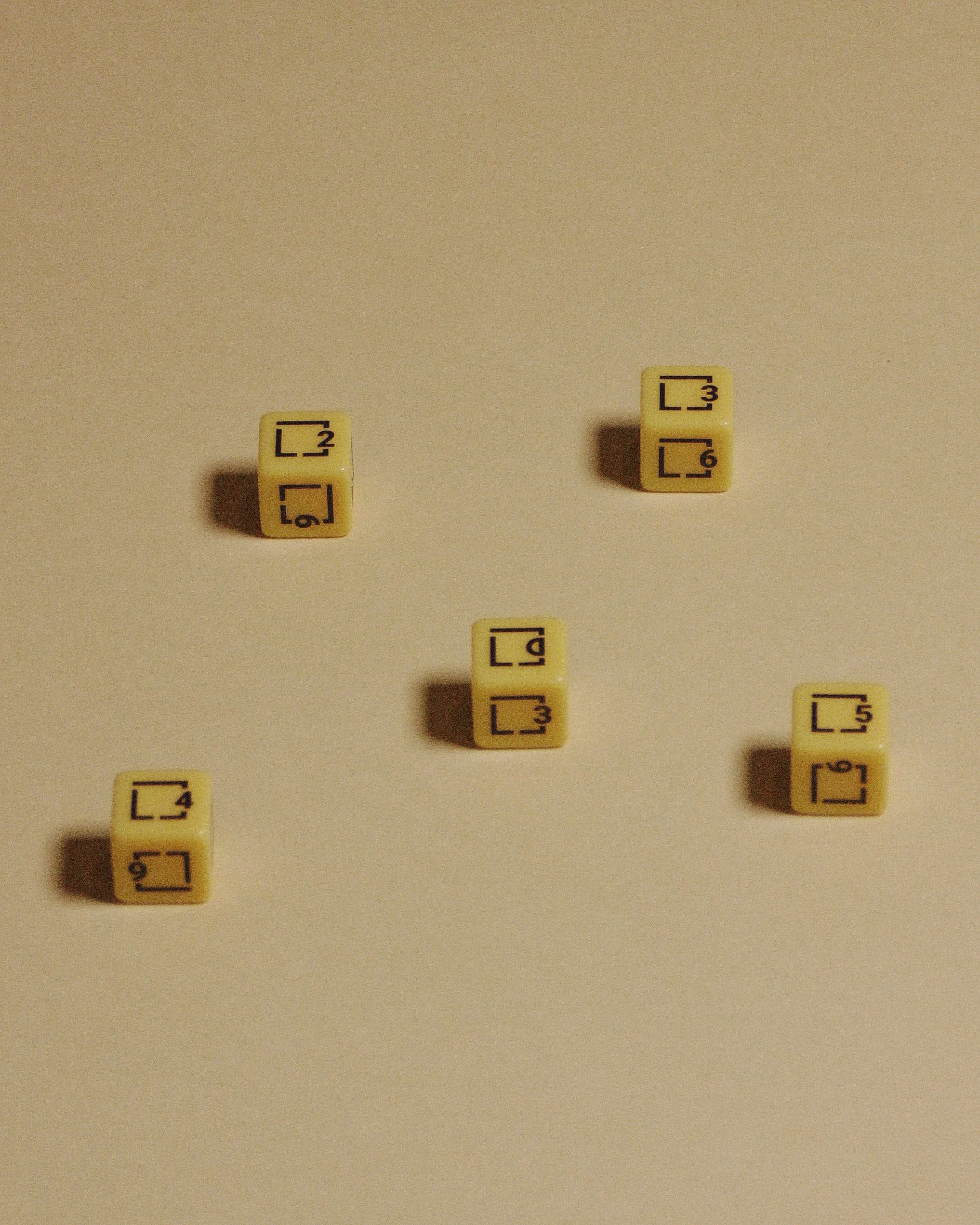 Five yellow dominoes with black symbols and numbers on a beige surface, casting shadows.