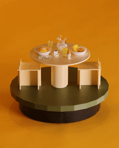 Miniature cafe display with a round table, chairs, and small food and drink items on a yellow background.