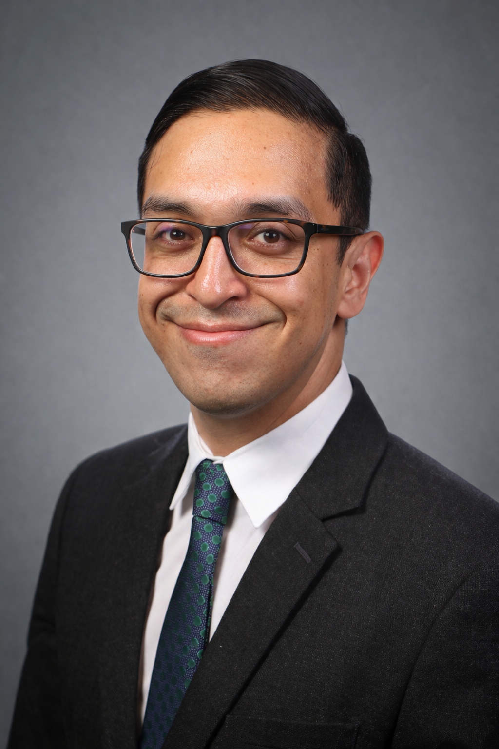 Cardiólogo con gafas, sonriendo, vestido con saco y corbata sobre fondo gris – retrato profesional médico, Dr Fabio Parada