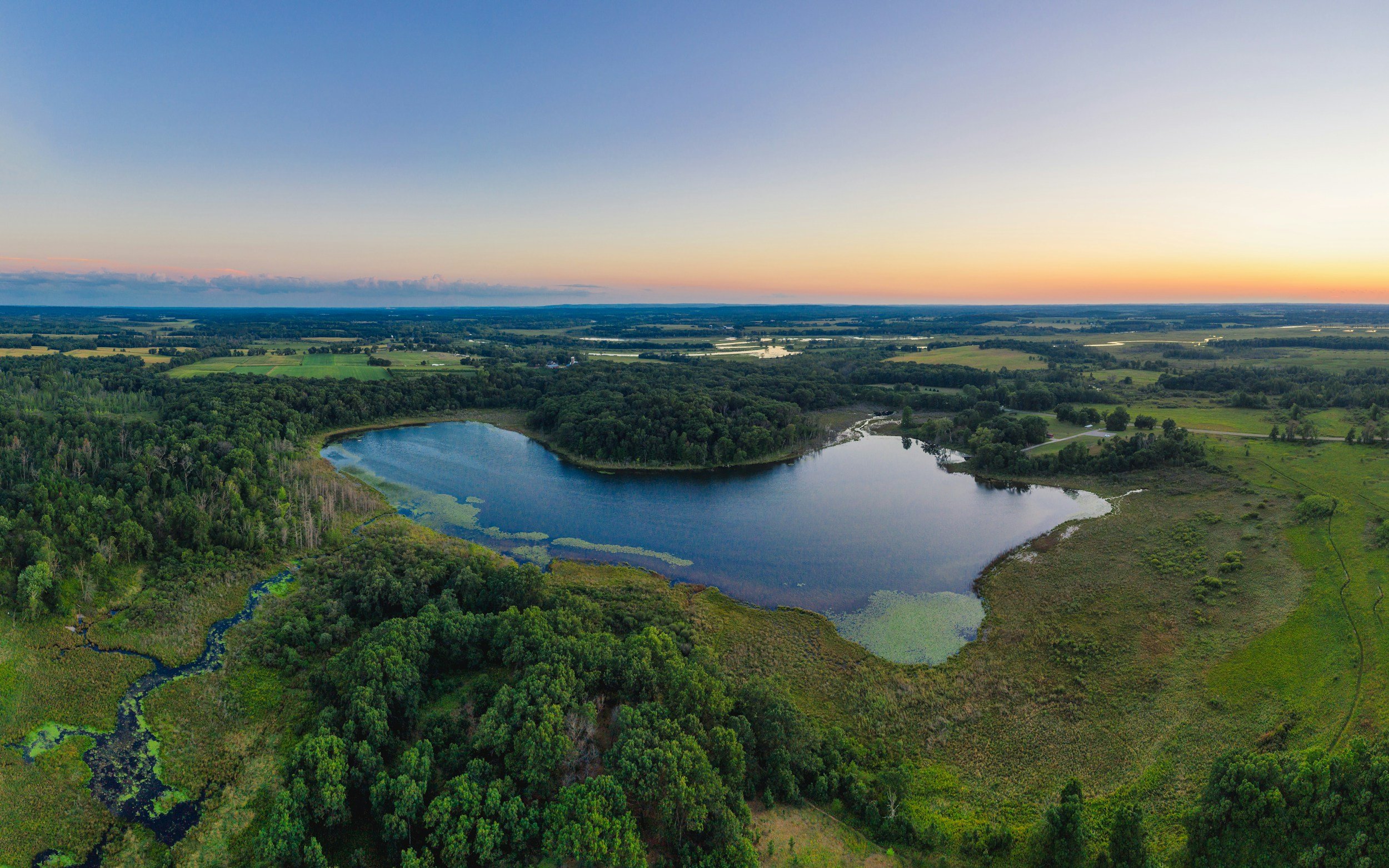 Aerial view of North and South Twin Lakes surrounded by lush green forests under a clear sky at sunset.
