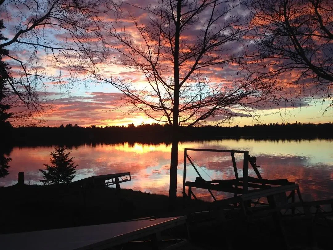 Scenic sunset over North Twin Lake with silhouetted trees and a dock in the foreground. The sky is vibrant with shades of orange, pink, and purple, reflecting off the water.