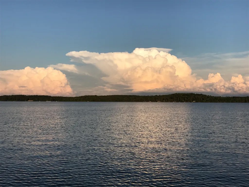 North Twin Lake with distant forest and large cumulonimbus clouds in the sky during sunset.