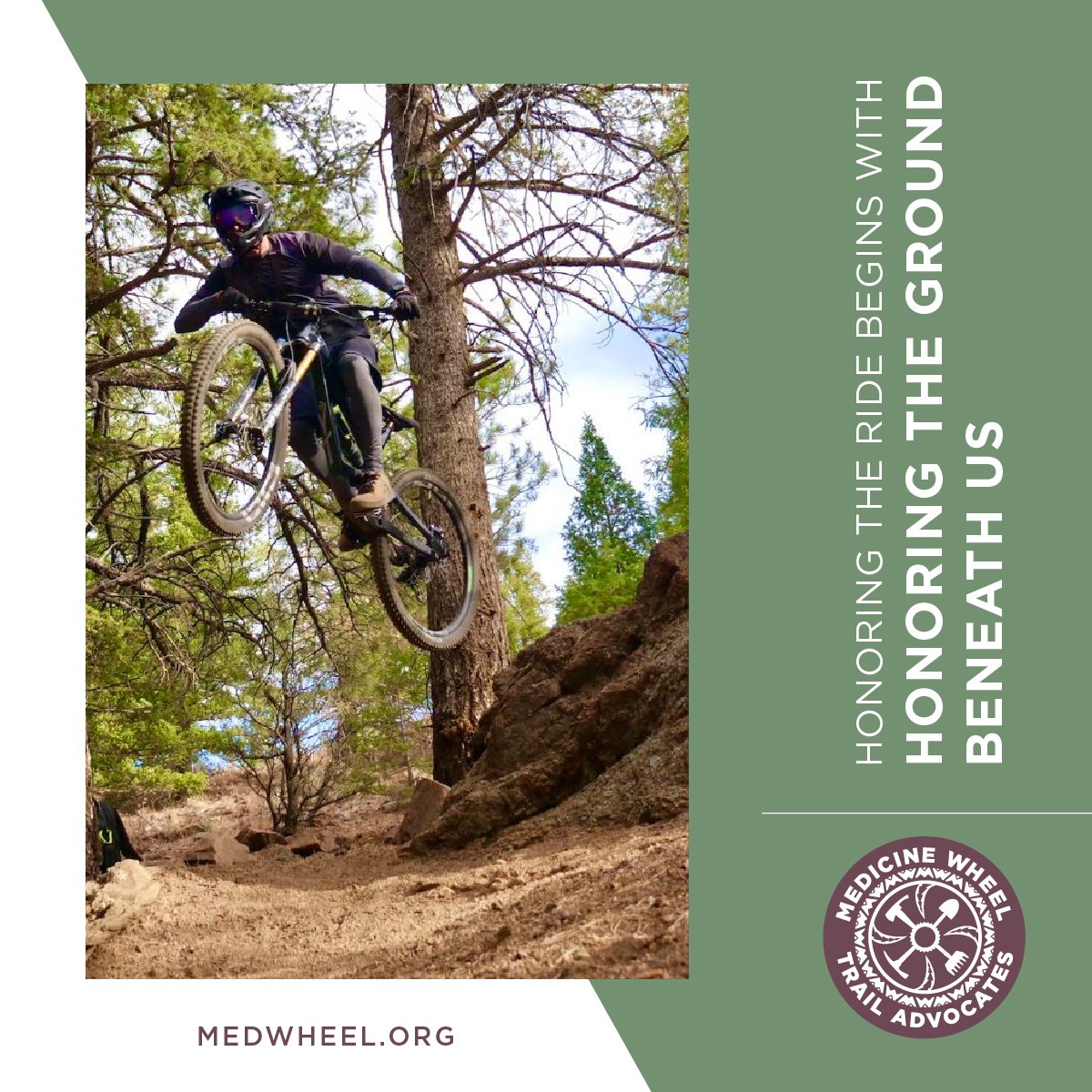 Person mountain biking off-road on a trail surrounded by trees, with rocks and dirt, wearing a helmet and protective gear.