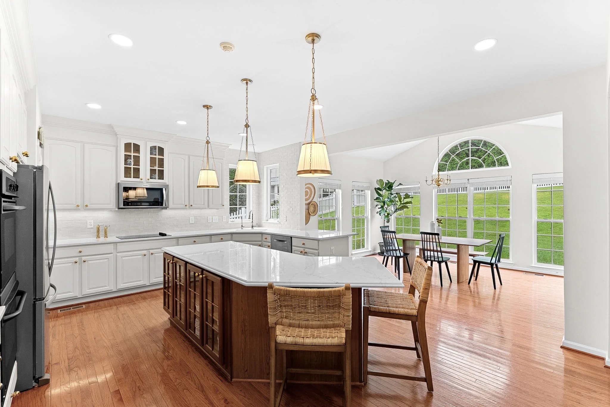 Spacious kitchen with white cabinetry, a large island with a white marble countertop, and a separate dining area with a large window and green outdoor view.