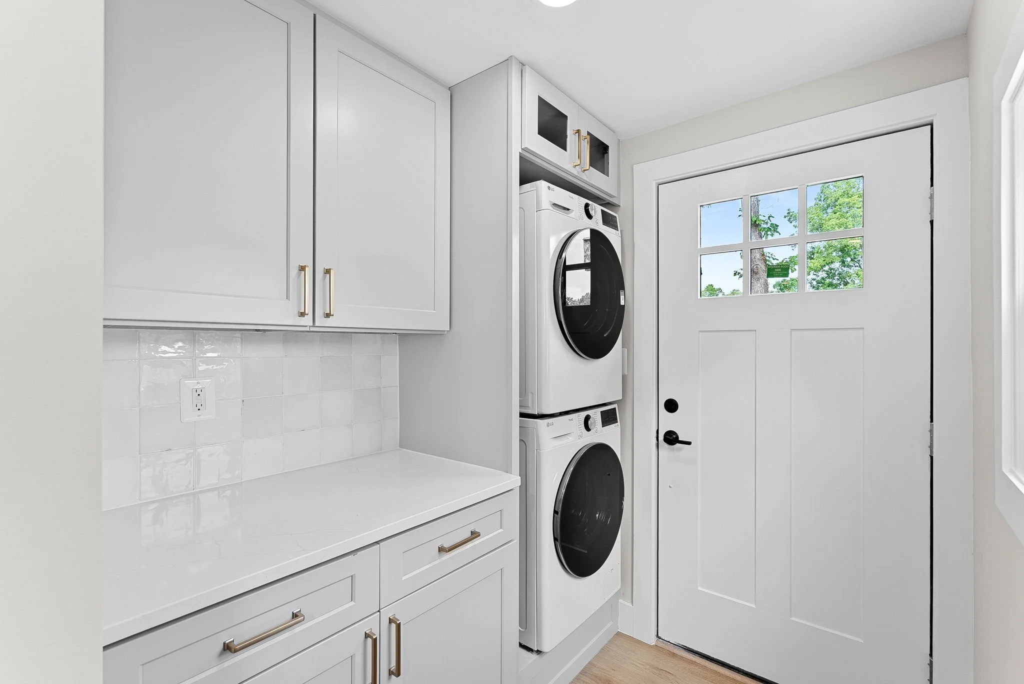 Clean laundry room with white cabinets and a stacked washer and dryer next to a white door with glass panels