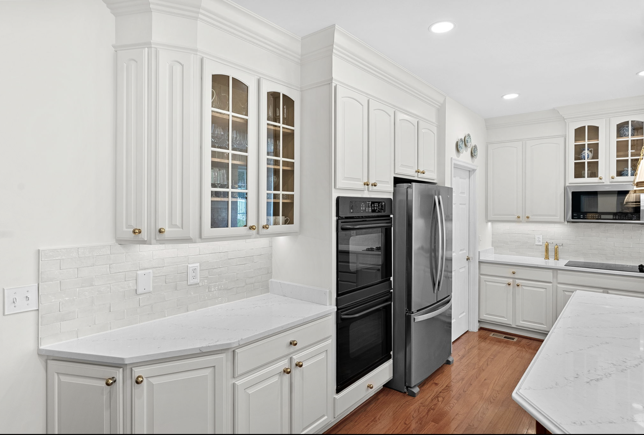 White kitchen with white cabinets, marble countertops, stainless steel appliances, and hardwood floors.