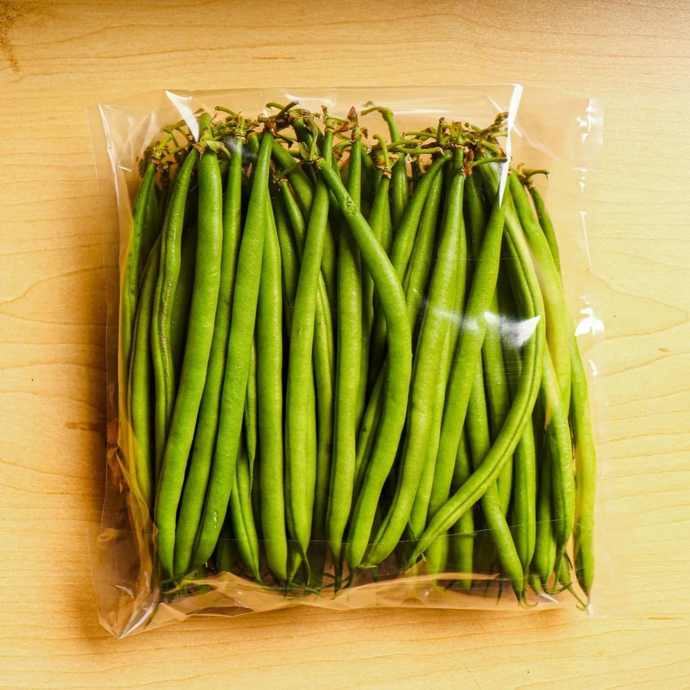 Fresh green beans in a clear plastic bag on a wooden surface.