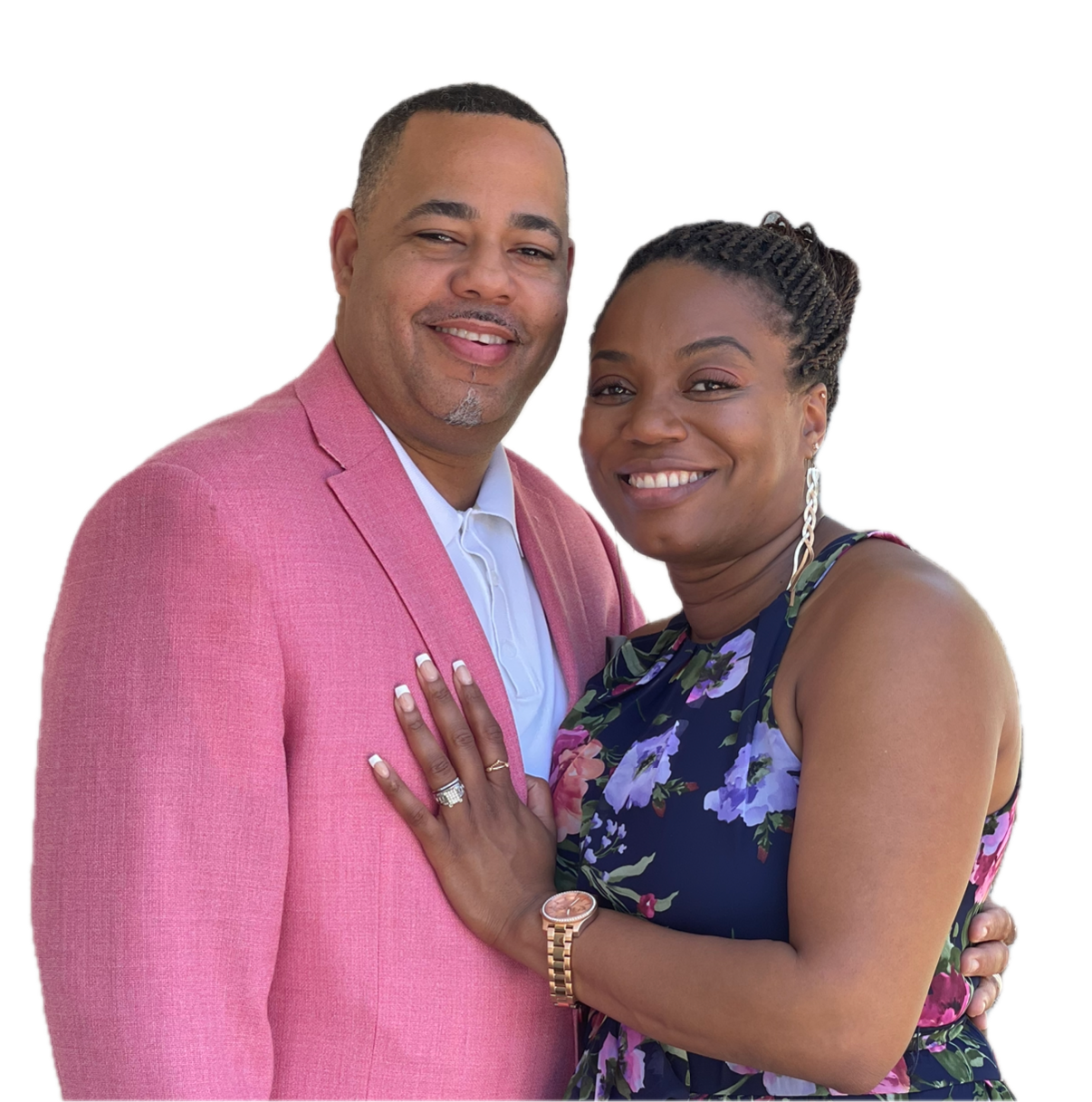 A smiling black man and woman standing close together, the woman touching the man's chest, both dressed nicely for a photo, with the woman wearing a floral dress and the man in a pink blazer.