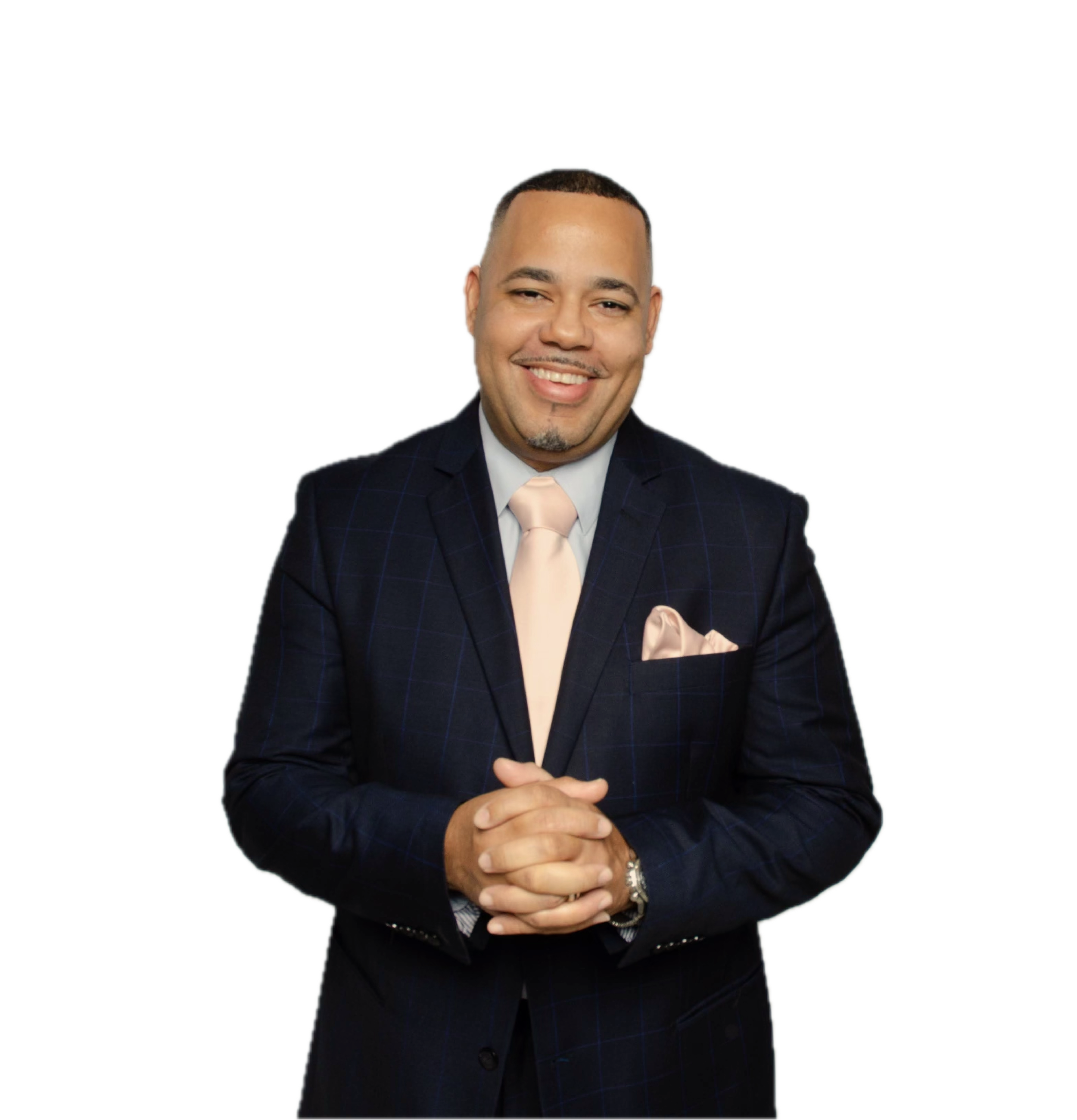 A man in a dark checkered suit with a light-colored tie and pocket square is smiling and has his hands clasped together.