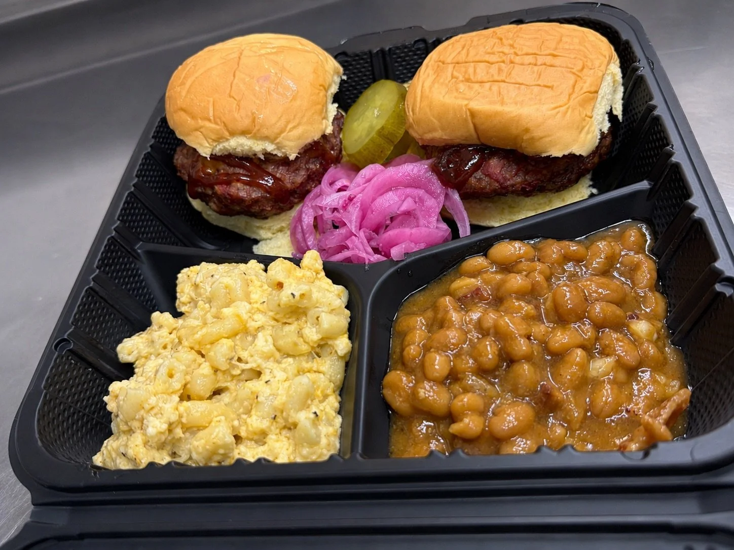 Smoked Meatloaf Sliders Plate with Baked Beans and Macaroni & Cheese garnished with Pickled Onions and Sweet & Spicy Pickles