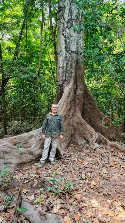 Alexandre Rago wildlife photographer standing beside the large roots of a tree in the Amazon rainforest, on an island in the Anavilhanas reserve, Brazil.