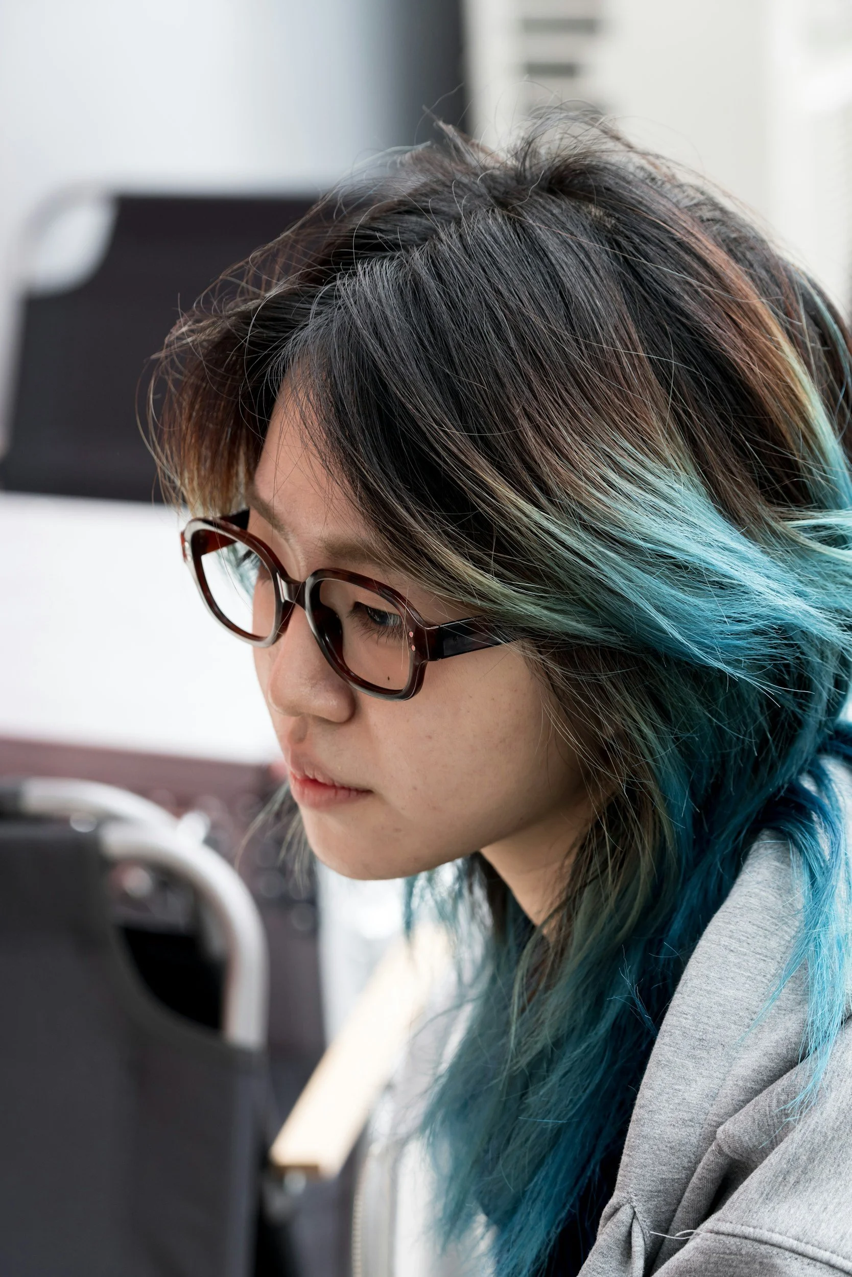 A woman with striped hair in shades of black, brown, and blue, wearing glasses, working on a computer.