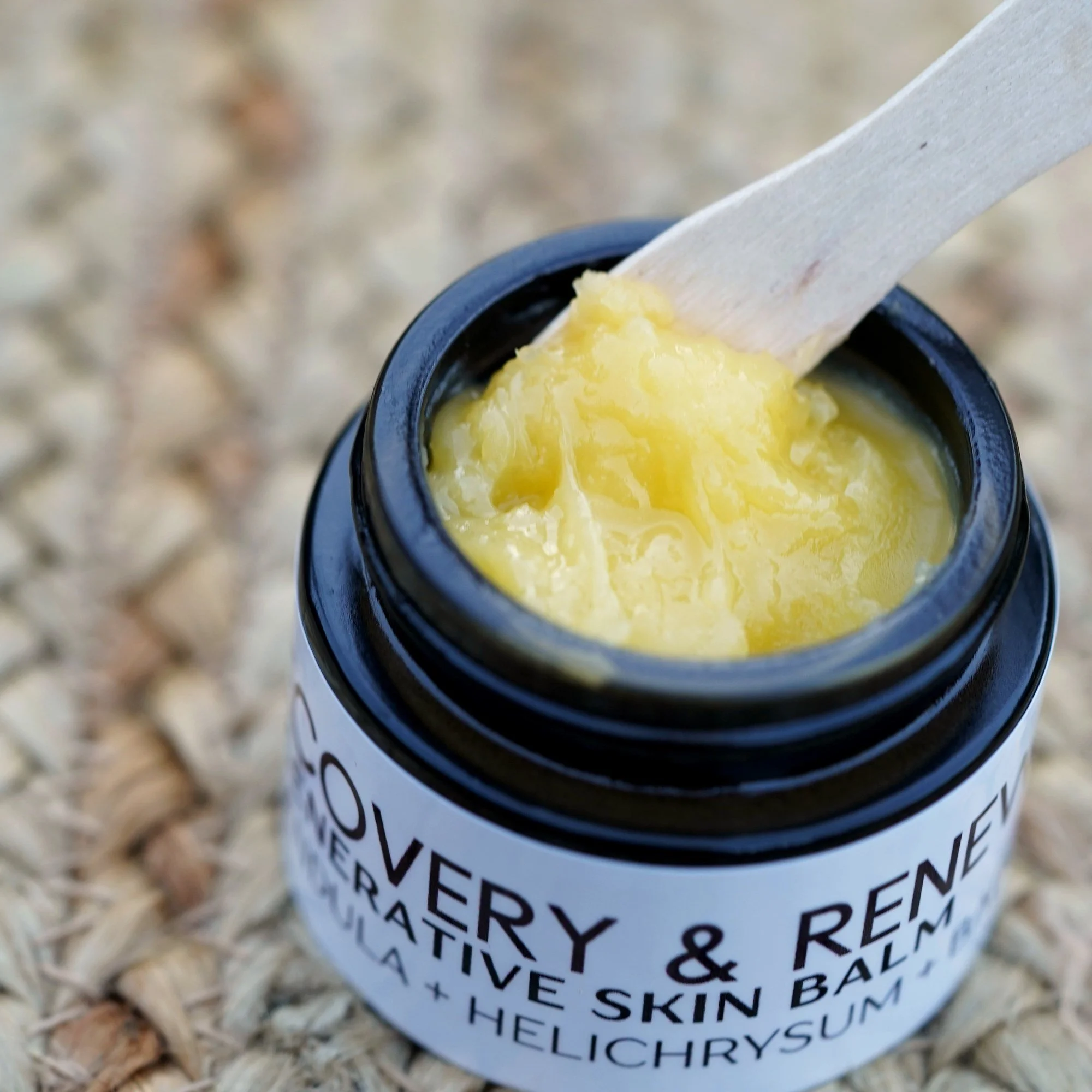Close-up of the rich golden texture of AliBee Recovery + Renewal Balm in a black glass jar