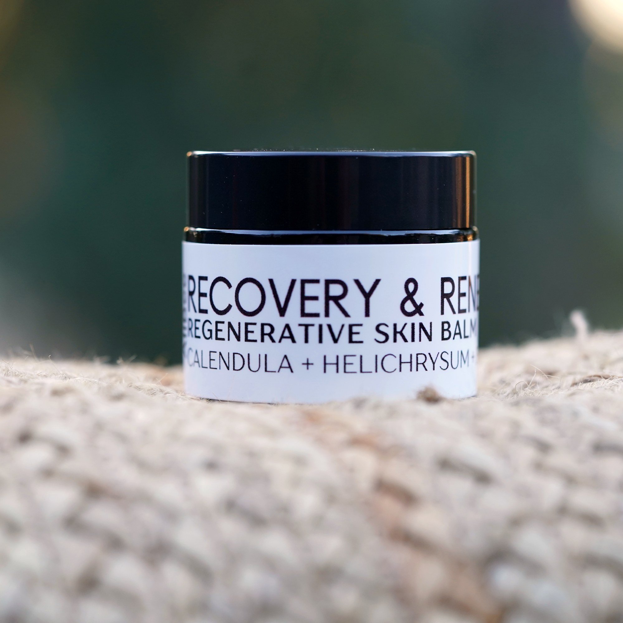 Closed 1 oz black glass jar of AliBee Recovery + Renewal Balm on a woven mat outdoors