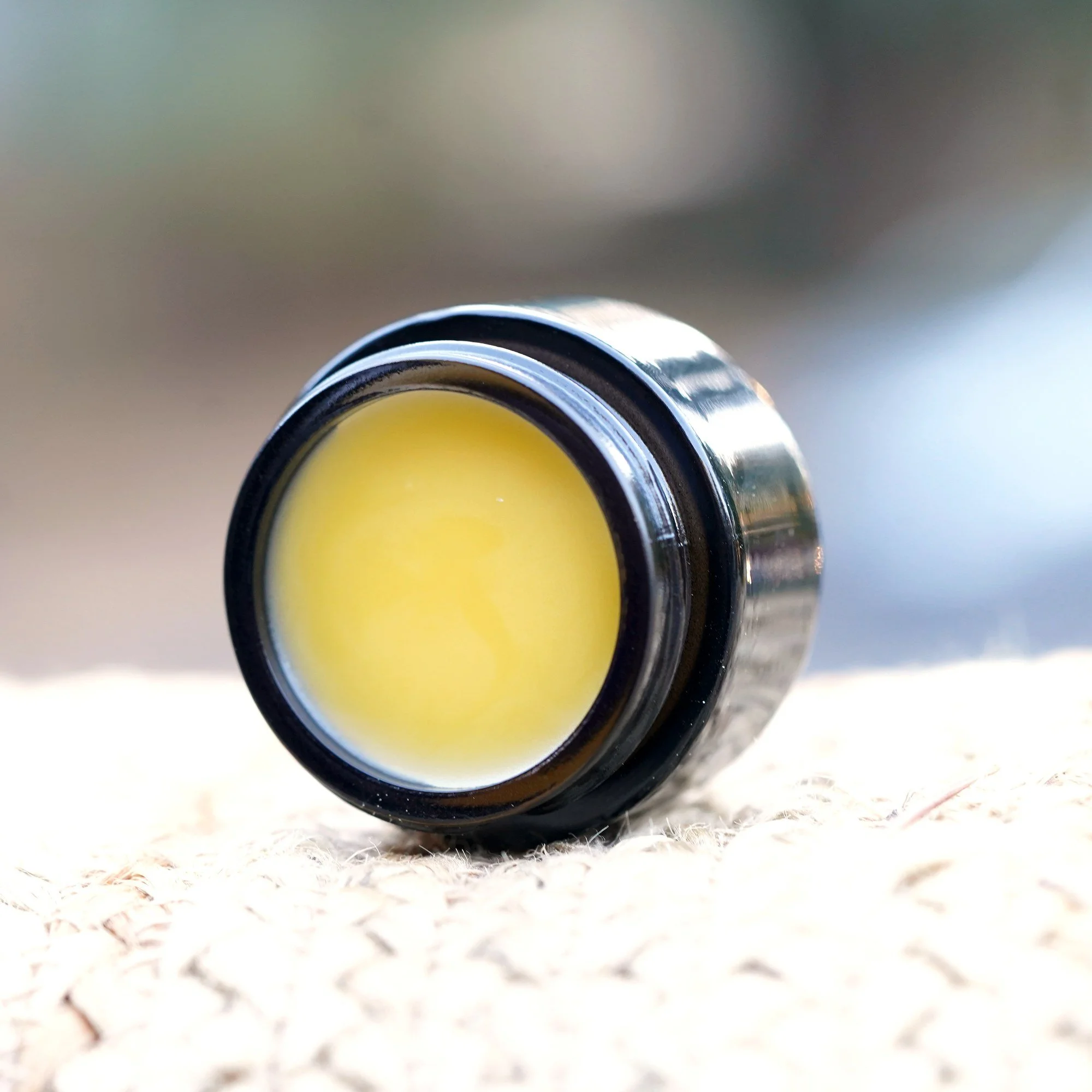 Open black glass jar of AliBee Recovery + Renewal Balm showing its smooth golden surface
