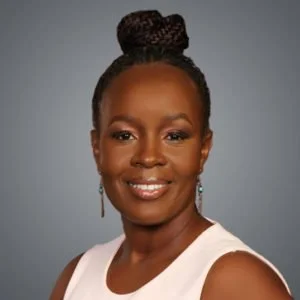 Portrait of a woman with braided hair bun wearing a sleeveless top and earrings, smiling, against a gray background.