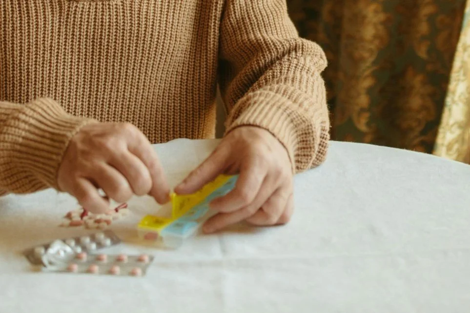 Person organizing pills in a weekly pill organizer on a table.