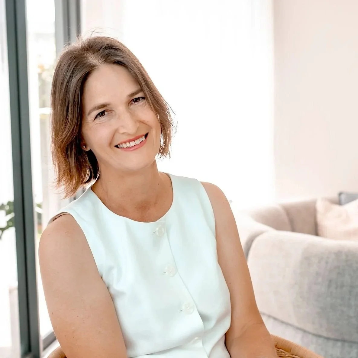 Jennifer - a woman with short brown hair smiling at the camera in a bright living room.